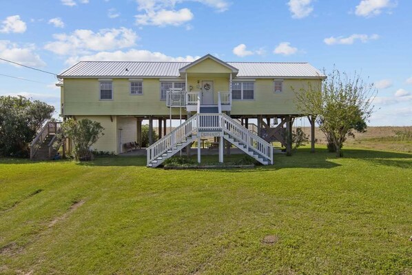 A two-story house with a front porch, a staircase leading to the entrance, and a small garden area. - Beach Life-Ruff E Nuff - Coastal Realty Group (Grand Isle)