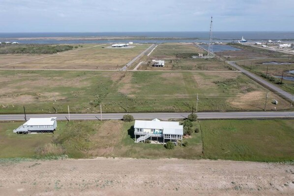 An aerial view of a coastal area with a prominent white building with a balcony, surrounded by open fields and a road. - Beach Life-Ruff E Nuff - Coastal Realty Group (Grand Isle)