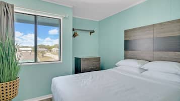 A bedroom with a bed, a nightstand, a window with curtains, and a view of the outside.