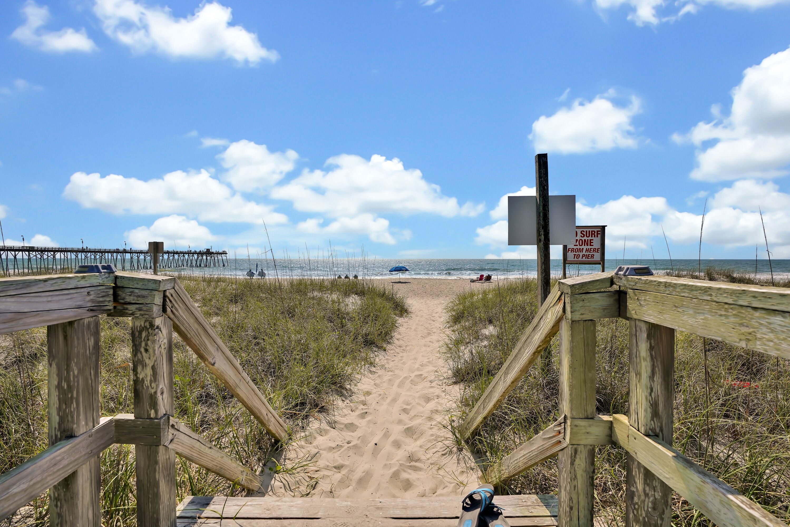 A wooden boardwalk leading to the beach with a sign indicating a surf zone.