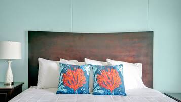 A neatly made bed with white linens and two decorative pillows with coral and sea life patterns.