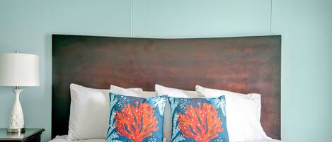 A neatly made bed with white linens and two decorative pillows with coral and sea life patterns.