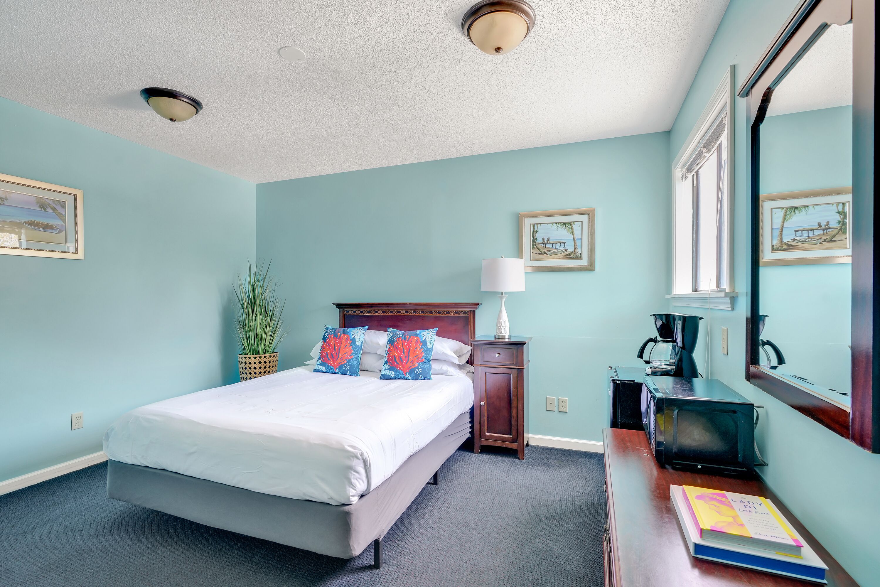 A neatly arranged bedroom with a bed, bedside table, lamp, and a book on a dresser.