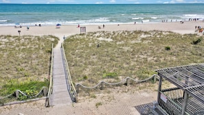 A beach with a wooden boardwalk leading to a wooden structure, surrounded by dunes and a clear sky. - Admiral's Quarter (Kure Beach)