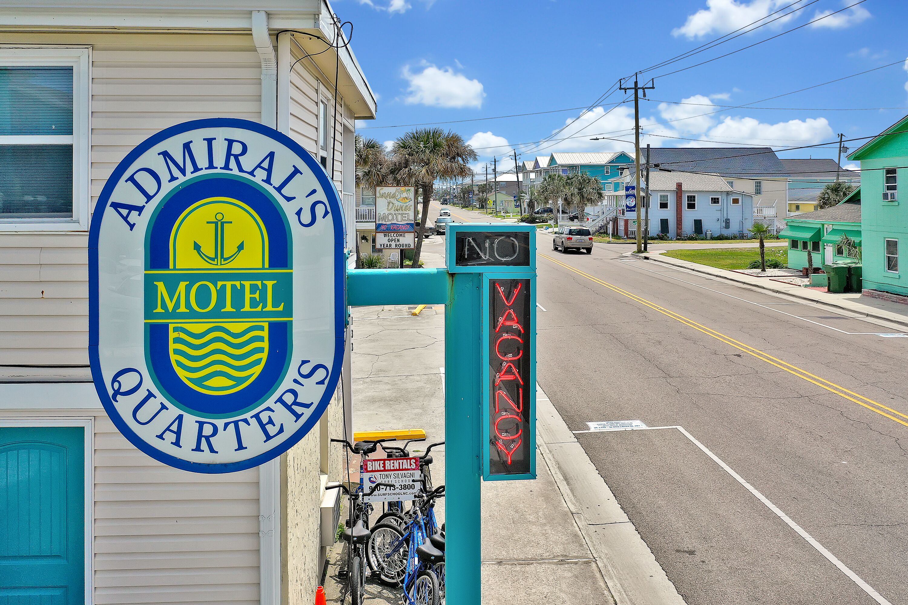A motel sign with a nautical theme, a bike rental sign, and a 'No Vacancy' sign.