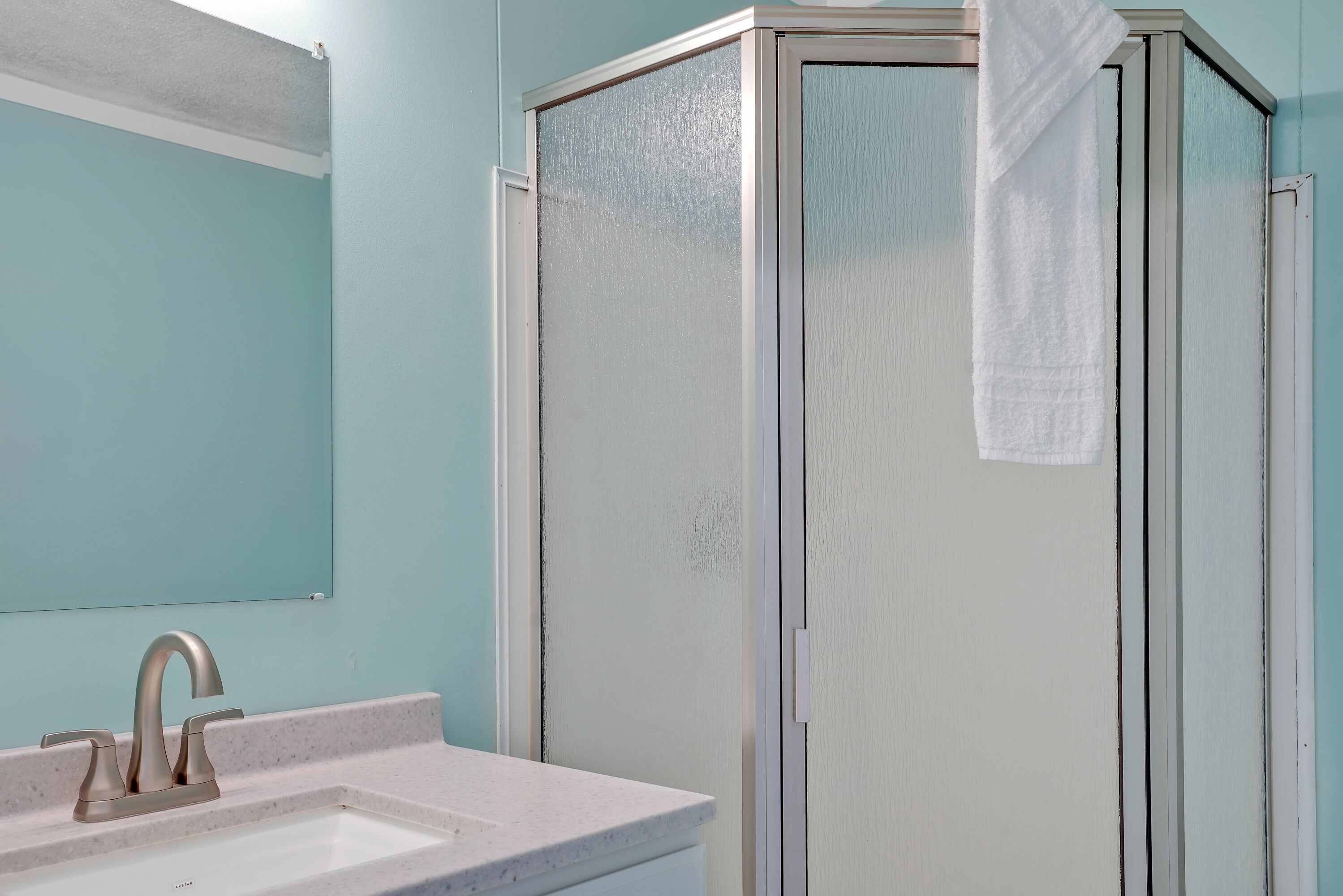 A bathroom with a sink, mirror, and a glass shower enclosure.