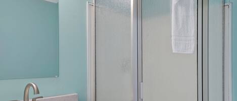 A bathroom with a sink, mirror, and a glass shower enclosure.