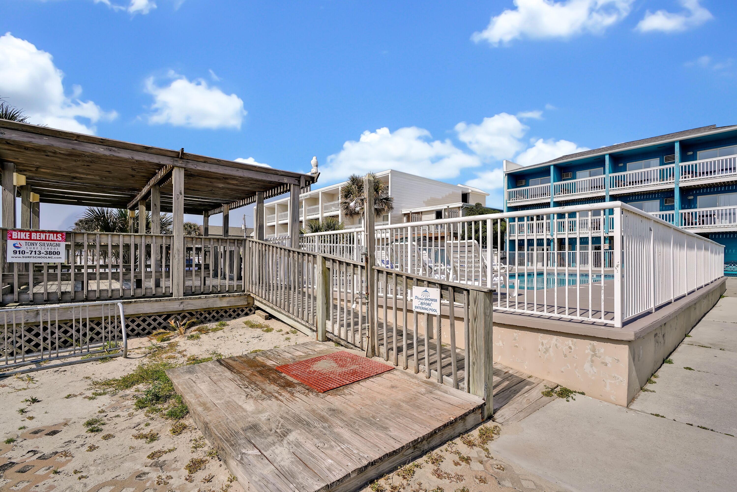 A beachfront property with a wooden deck, a sign for bike rentals, and a pool area.