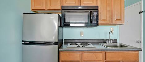 A compact kitchen with wooden cabinets, a stainless steel refrigerator, a microwave, and a gas stove.