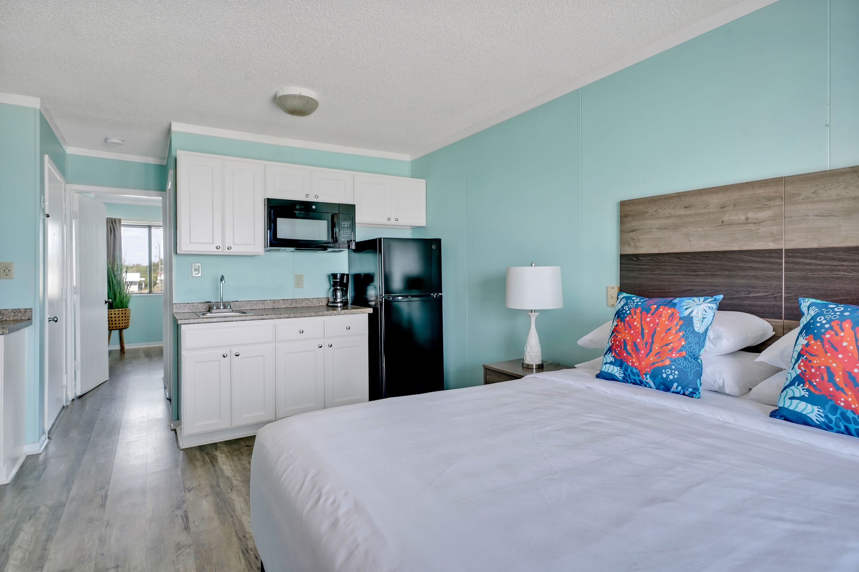 A hotel room with a bed, a nightstand, a lamp, a microwave, a refrigerator, and a kitchenette.