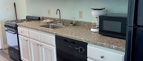 A modern kitchen with white cabinets, a granite countertop, a black dishwasher, a stove, and a microwave.