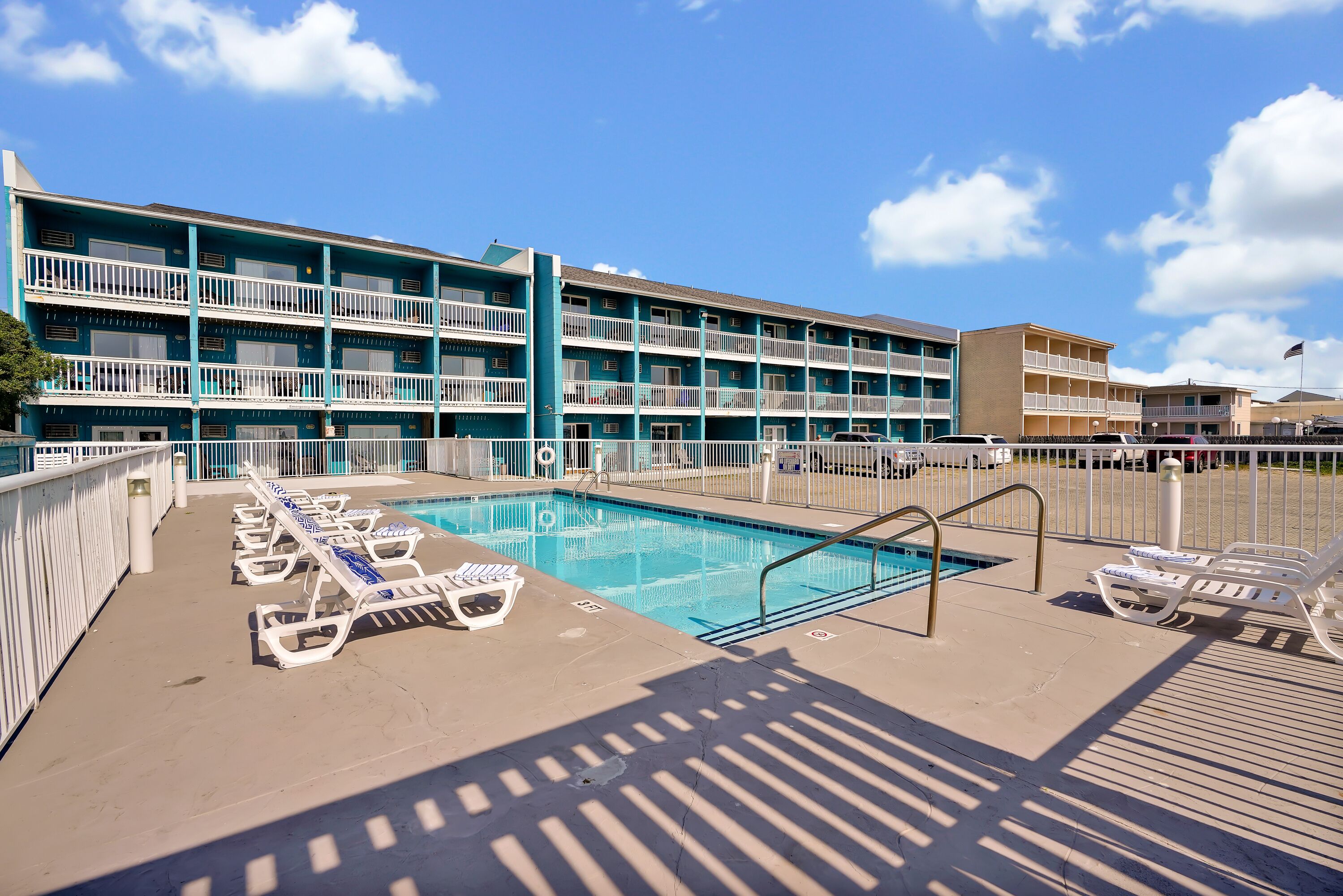 A pool area with lounge chairs and a building with multiple balconies.