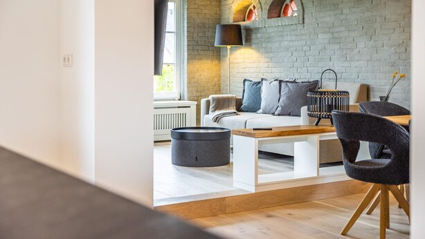 A modern living room with a stone wall, a sofa, a coffee table, and a lamp. - Sylt Seascape IV - HoogeBay - High-quality luxury house for 6 people with sauna, (Sylt)