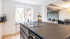 A modern kitchen with a central island, a built-in oven, and a window overlooking a garden. - Sylt Seascape IV - HoogeBay - High-quality luxury house for 6 people with sauna, (Sylt)