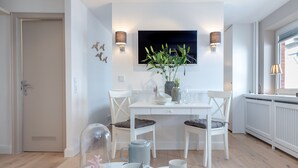 A modern dining area with a white table, two chairs, a potted plant, and a TV mounted on the wall.