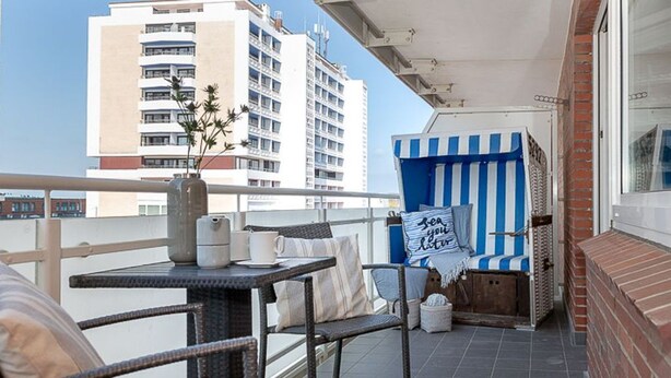 A balcony with wicker furniture, a striped blue and white chair, and a view of a tall building.