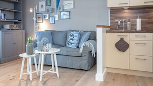 A modern living room with a grey sofa, a small white table, and a kitchen area with wooden cabinets and a countertop.