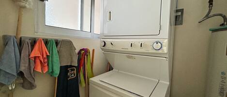 A compact laundry room with a front-loading washer and dryer, a window above the dryer, and a towel rack with various towels.