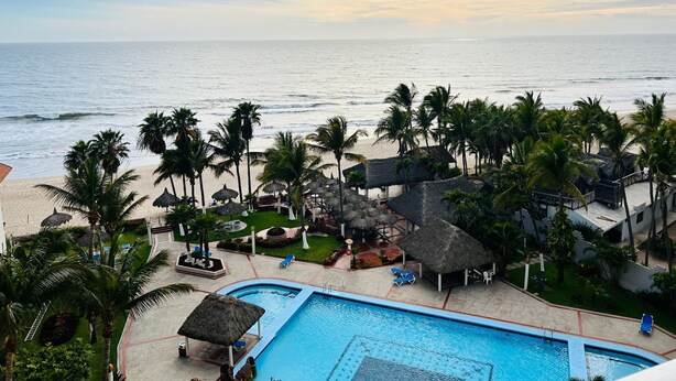 Un resort con piscina, playa y palmeras.