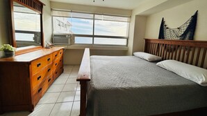 Un dormitorio con cama, cómoda de madera, ventanas amplias y ventilador de techo.