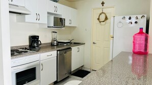 Una cocina con gabinetes blancos, microondas, cafetera, licuadora, lavavajillas y refrigerador.