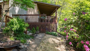 A covered porch with a wooden railing, surrounded by lush greenery and flowering plants. - Great Grandfather View - hot tub, fire pit, family games, all bedrooms on main level, views (Banner Elk)