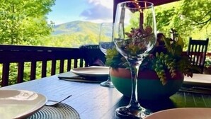 A table set outdoors with a view of green hills, a glass of water, and a bowl of fruit. - Great Grandfather View - hot tub, fire pit, family games, all bedrooms on main level, views (Banner Elk)