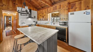 A wooden cabin-style kitchen with a central island, bar stools, and a refrigerator. - Great Grandfather View - hot tub, fire pit, family games, all bedrooms on main level, views (Banner Elk)