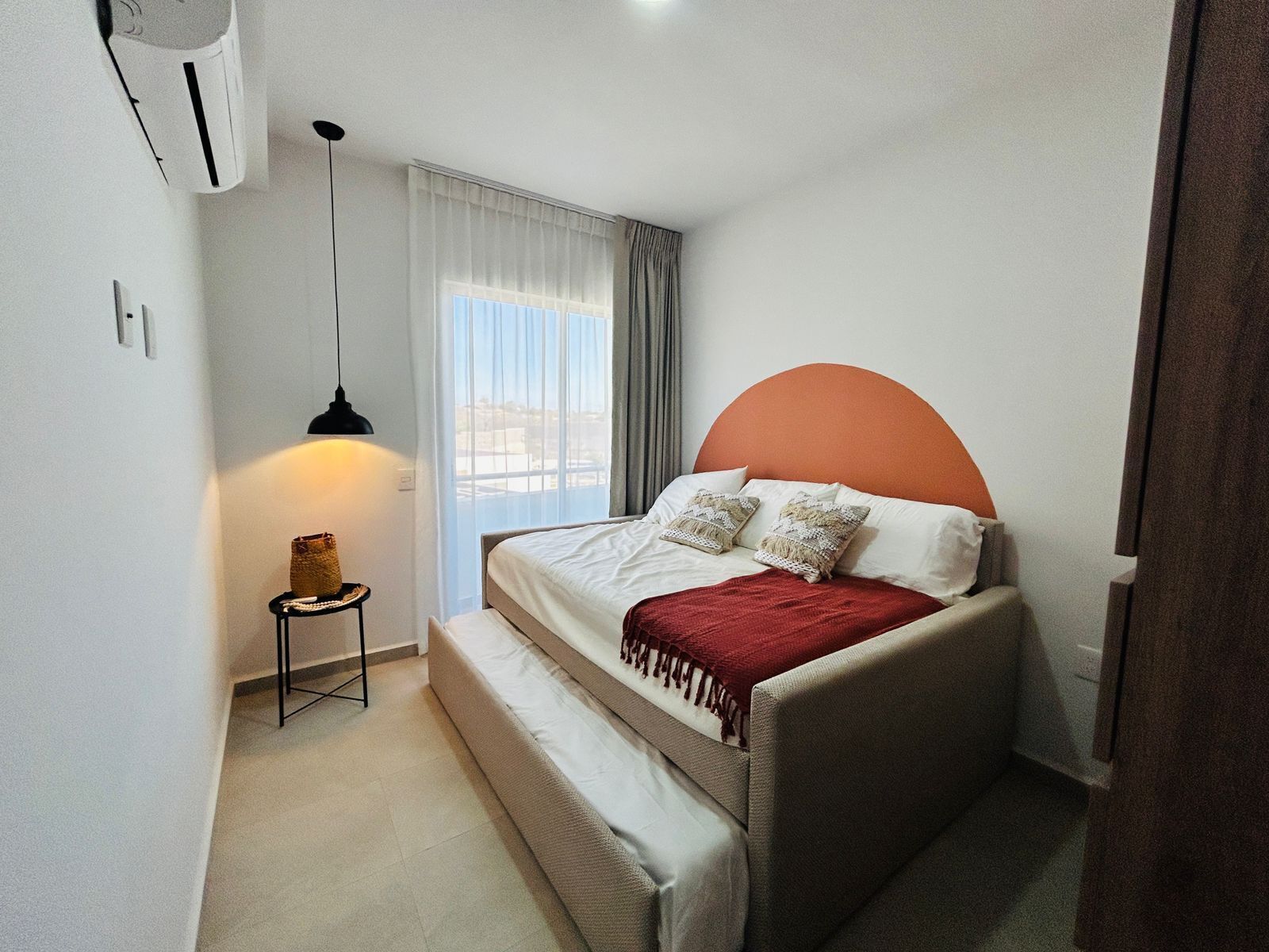 A bedroom with a bed, a bedside lamp, a small table, and a window with curtains.