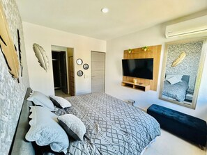 A modern bedroom with a large bed, a TV mounted on the wall, and a mirror reflecting the bed.