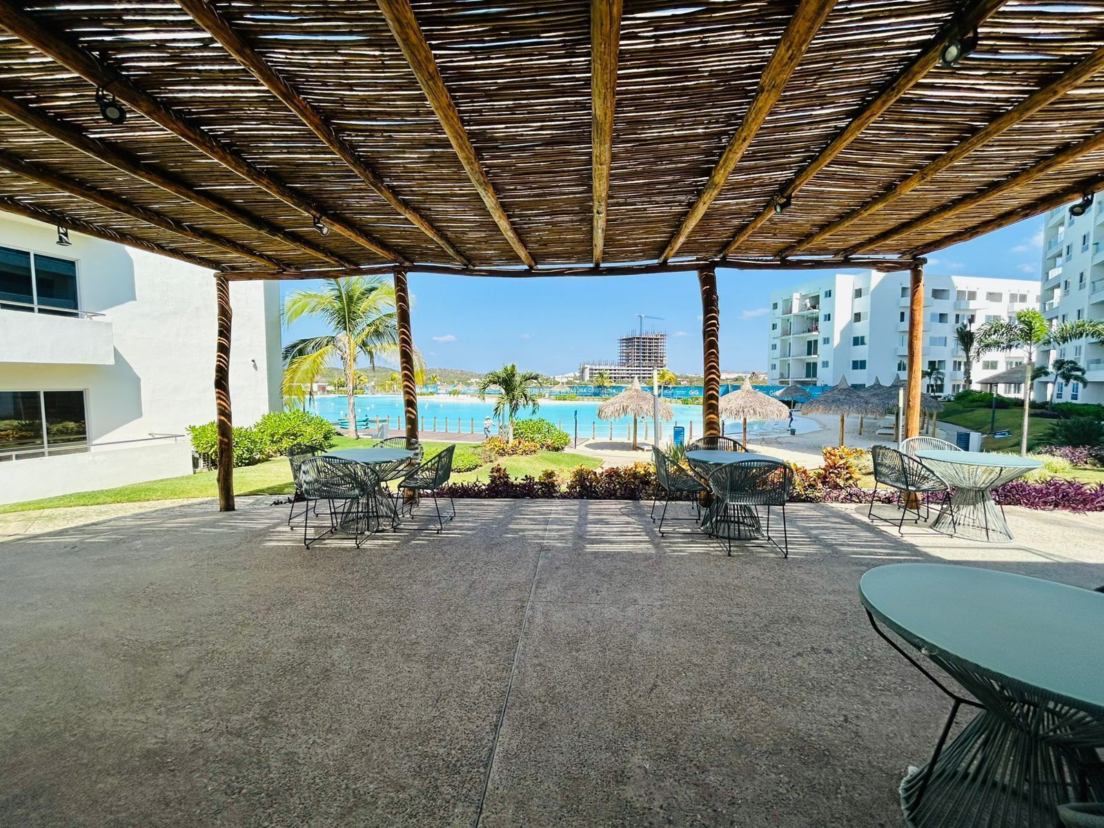 A covered outdoor area with tables and chairs, overlooking a pool and a beach.