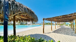A beach with a pool, thatched umbrellas, and lounge chairs. - Blue Lagoon (Mazatlán)