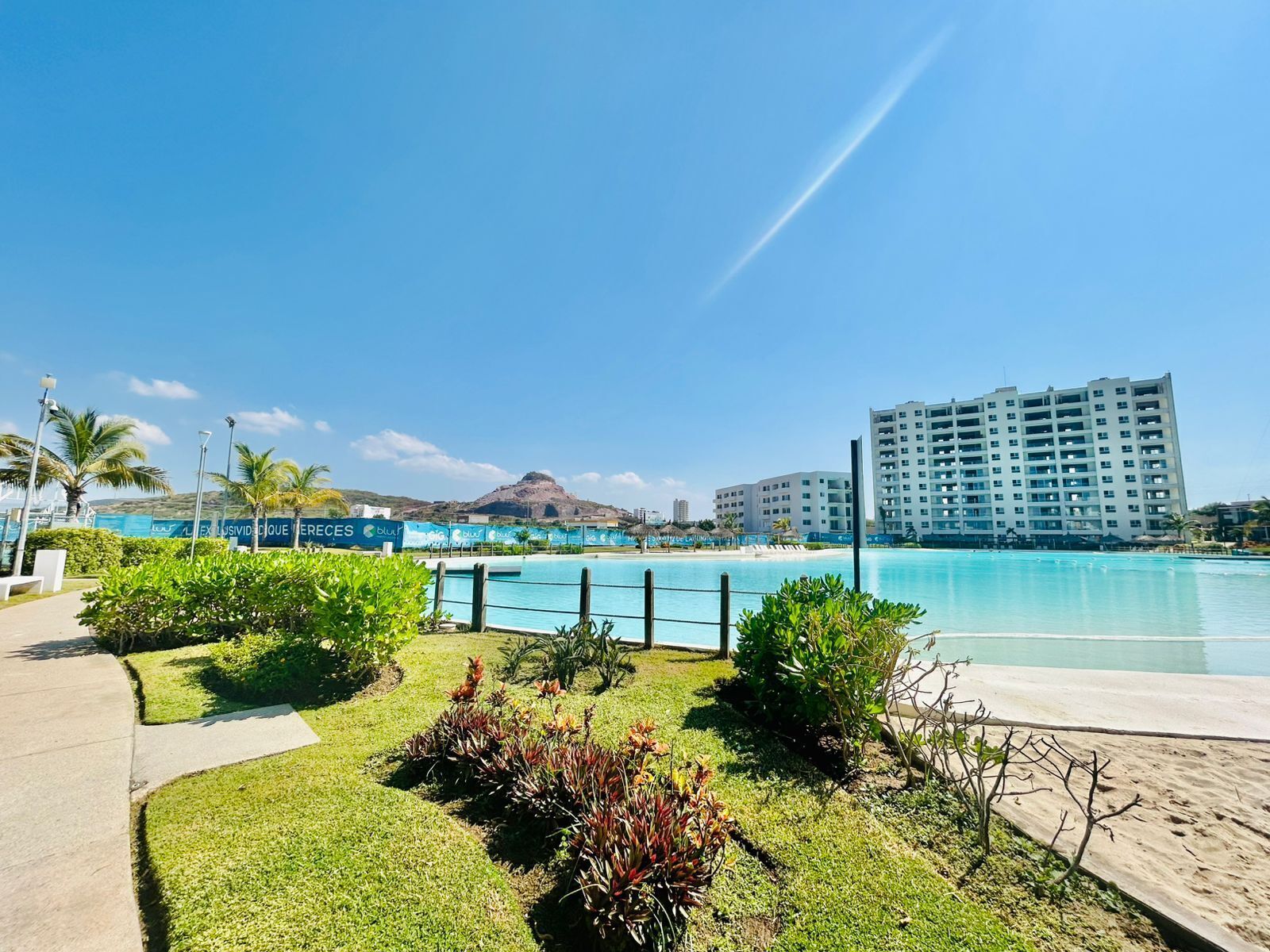 Un resort con una gran piscina, una zona de playa y una montaña al fondo.