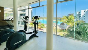 A gym with exercise equipment and large windows overlooking a pool and resort area. - Blue Lagoon (Mazatlán)