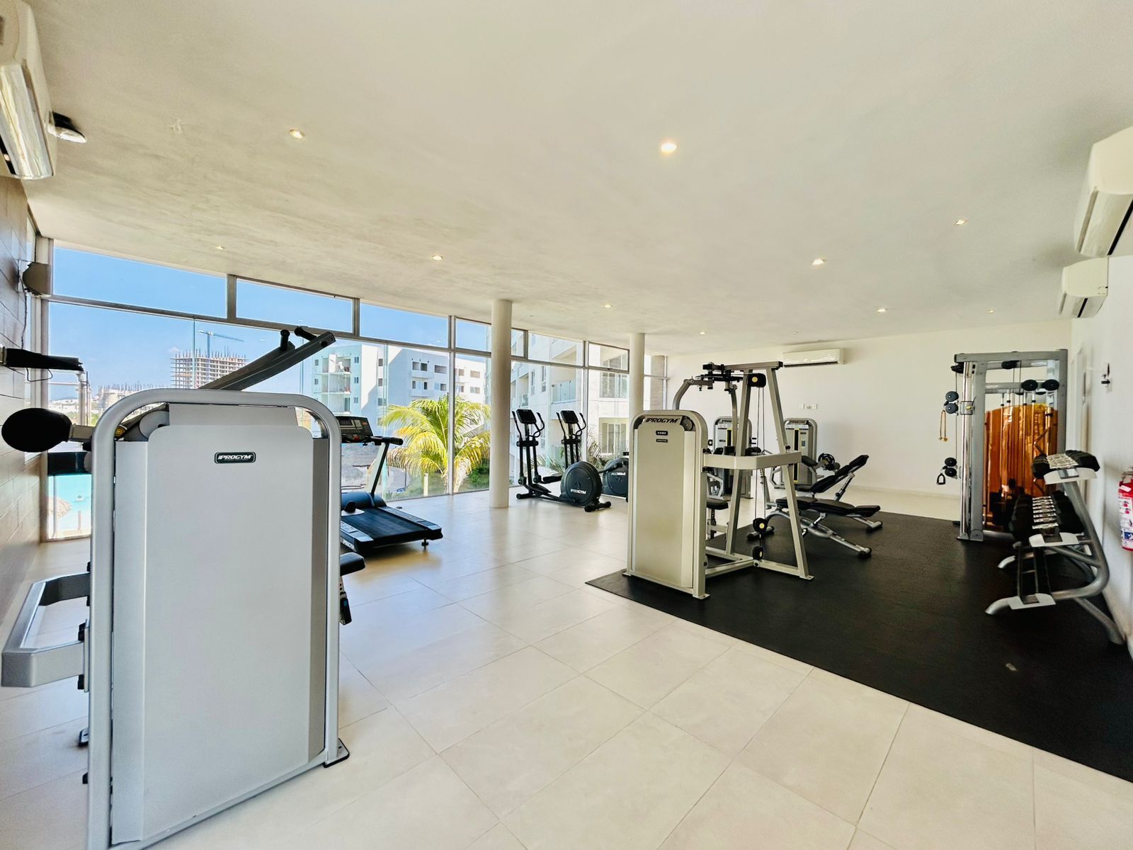 A spacious gym with various exercise equipment, large windows offering views of the city, and a modern interior design.