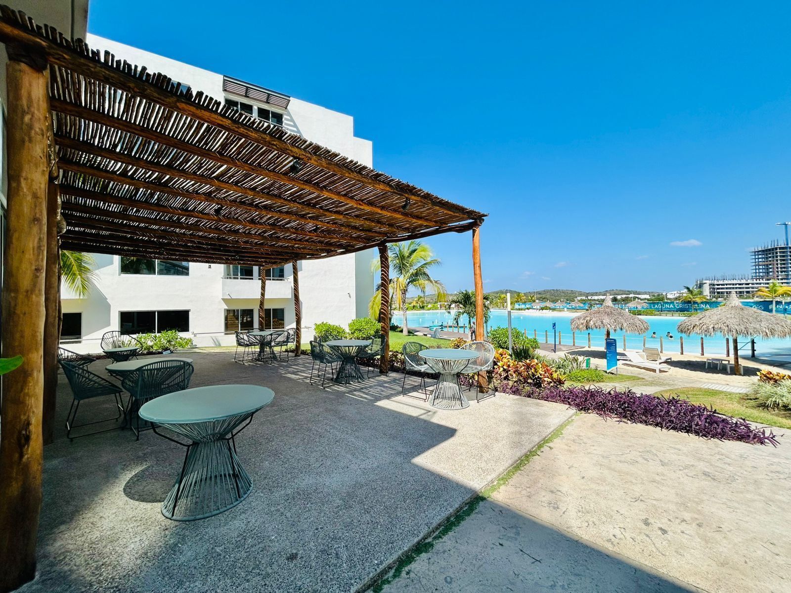 Un patio al aire libre con mesas y sillas, una piscina al fondo y vistas a la costa.
