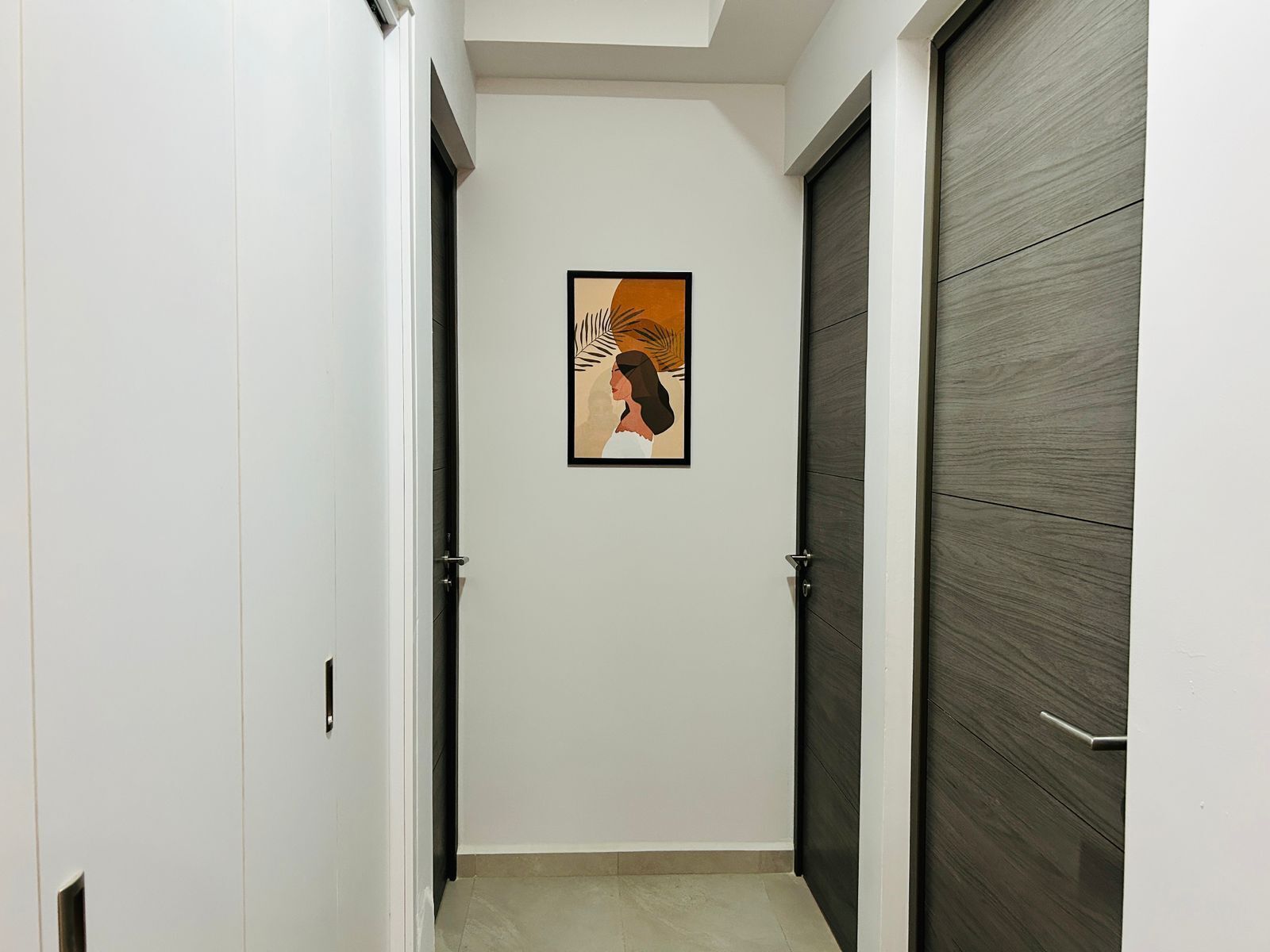 A hallway with a framed artwork on the wall, a door on the right, and a door on the left.