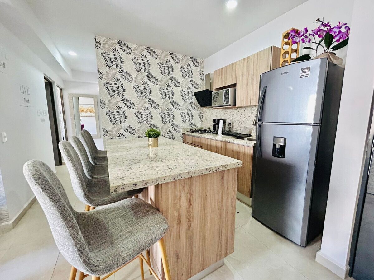 A modern kitchen with a granite countertop, wooden cabinets, and a stainless steel refrigerator.