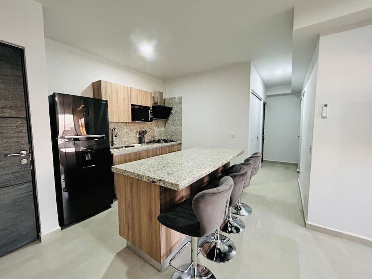 Eine moderne Küche mit einem schwarzen Kühlschrank, Holzschränken, Granitarbeitsplatten und Barhocker.
