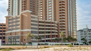 A high-rise hotel with multiple floors, balconies, and a parking garage. - Phoenix Gulf Towers 802 | Beachfront | Spectacular Gulf Views | Pools | My Beach Getaways (Orange Beach)