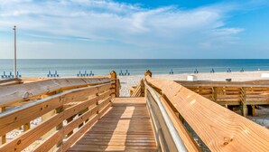 A wooden boardwalk leading to a beach with blue chairs and umbrellas. - Phoenix Gulf Towers 802 | Beachfront | Spectacular Gulf Views | Pools | My Beach Getaways (Orange Beach)