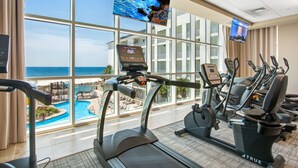 A fitness center with treadmills, stationary bikes, and an elliptical machine, overlooking a pool and ocean view. - Phoenix Gulf Towers 802 | Beachfront | Spectacular Gulf Views | Pools | My Beach Getaways (Orange Beach)