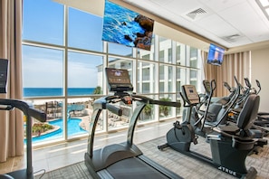 Un gimnasio con cintas de correr, bicicletas estáticas y una máquina elíptica, con vistas a una piscina y al océano.