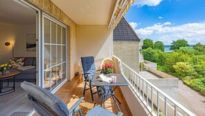 A balcony with a view of greenery and a body of water, furnished with a table, chairs, and a sofa. - fewo1846 - South view (App. 689) / Studio apartment with balcony on the mezzanine floor - (Harrislee)