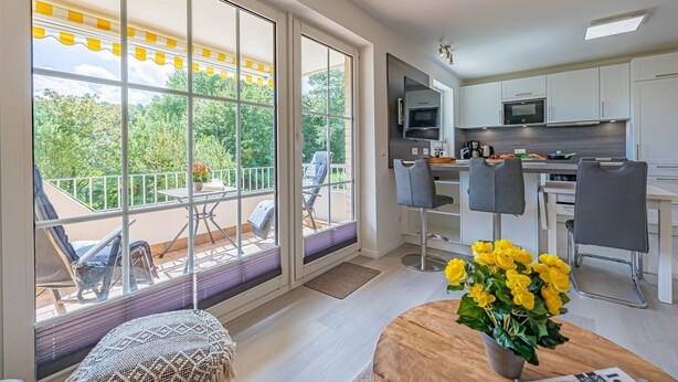 A modern kitchen with a dining area, large windows, and a balcony with outdoor seating. - fewo1846 - South view (App. 689) / Studio apartment with balcony on the mezzanine floor - (Harrislee)