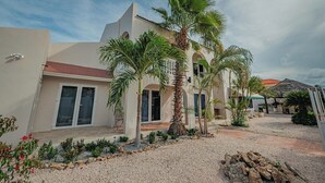 A modern building with a courtyard, palm trees, and a gravel pathway. - Villa de Leon, suitable for 14 persons. 5 bedrooms, 5 bathrooms (Noord)