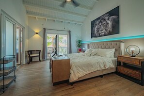 A spacious bedroom with a large bed, a desk, and a chair. There is a window with curtains, a plant, and a painting of a lion on the wall. - Villa de Leon, suitable for 14 persons. 5 bedrooms, 5 bathrooms (Noord)