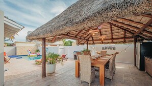 A patio area with a thatched roof, a pool, and outdoor furniture. - Villa de Leon, suitable for 14 persons. 5 bedrooms, 5 bathrooms (Noord)