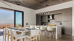 Een moderne keuken met een groot schiereiland, een eethoek met witte stoelen, en uitzicht op het woestijnlandschap.
