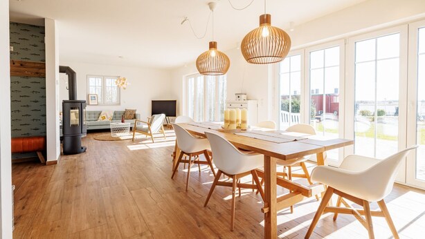 Ein modernes Wohnzimmer mit Kamin, einem Essbereich mit Holztisch und Stühlen und großen Fenstern mit Blick ins Freie.